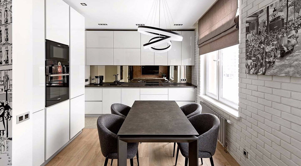 Сделанную на заказ кухню отличает необычный зеркальный фартук и столешница из натурального гранита. Кирпич­ная стена у окна окрашена под цвет кухонных фасадов.