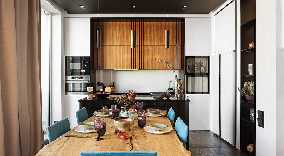 Осевая симметрия столовой и обеденной зон заостряет внимание на деталях: мощном массиве столешницы, заказанной в Краснодарском крае, выразительных окантовках кухонных шкафов.