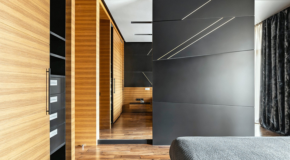 В спальне доминируют отделка деревом с медово-золотистыми поверхностями и антрацитно-чёрный цвет, прида­ющий интерьеру глубину. Облицовка зеркалами по высоте стен до самого потолка п...