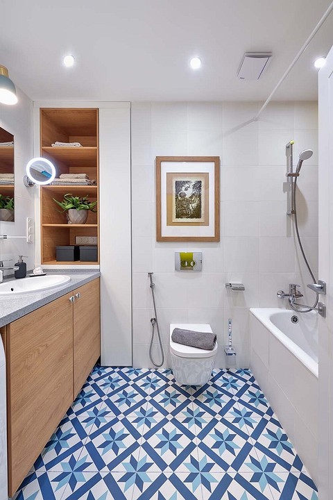 Синие узоры на напольной плитке и шпон дерева в отделке мебели, графика на стене внесли в стерильную рациональность дизайна ванной теплоту и индивидуальность.