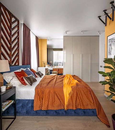 Оранжево-жёлтые покрывала, насыщенно жёлтые стены у зеркала и напротив кровати, а также живое растение в кашпо создают в спальне атмосферу солнечной осени.