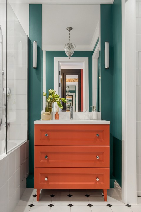 В ванной скомбинировано два активных цвета — коралловый и изумрудный (тумба, стены, штора). Контраст выглядит эффектно и уравновешен светлой плиткой. 