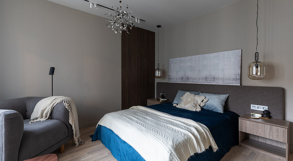 В спальне — длинное изголовье кровати, которое сделали из двух модулей. Но шва между ними не видно, для этого специально сшили чехол. Розетки по бокам от кровати встроены в само изго...