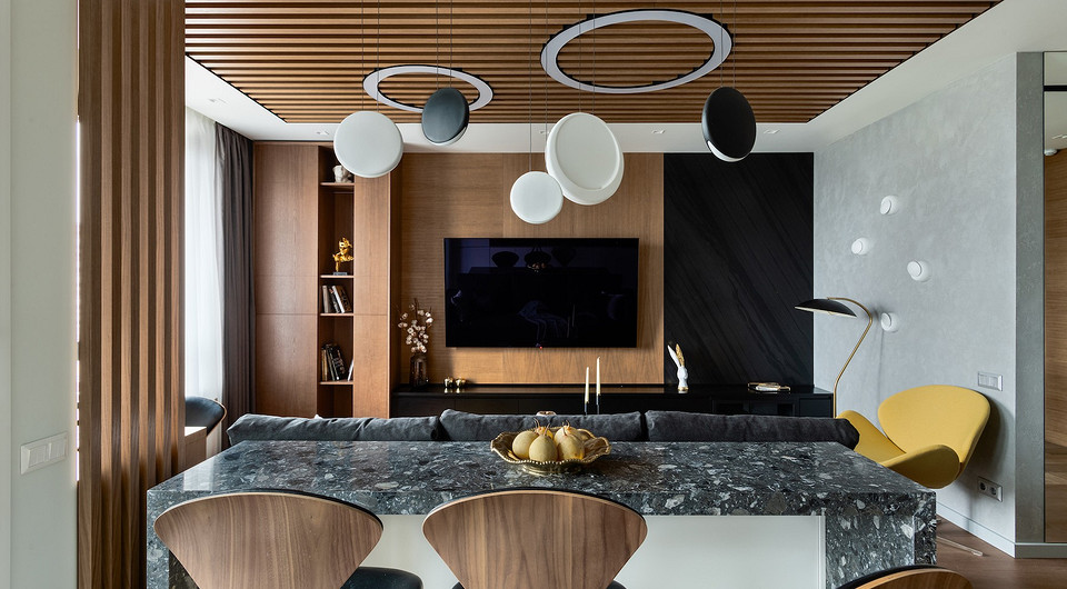 Вдоль стены в гостиной зоне расположена тумба со встроенным биокамином. Ее задекорировали деревянными панелями с фрезеровкой и скомбинировали со слэбом камня (натуральный сланец). 