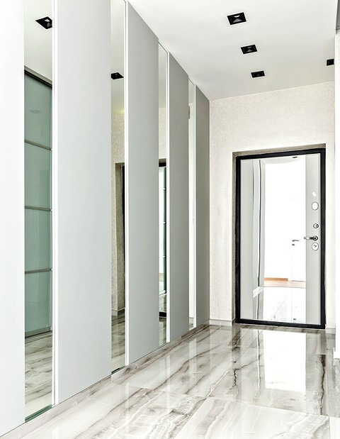 Чтобы узкий коридор казался шире, одну из стен оформили зеркалами в сочетании с панелями MDF, покрытыми светло-серой матовой эмалью. Всю отделку крепили на двухкомпонентный клей.
