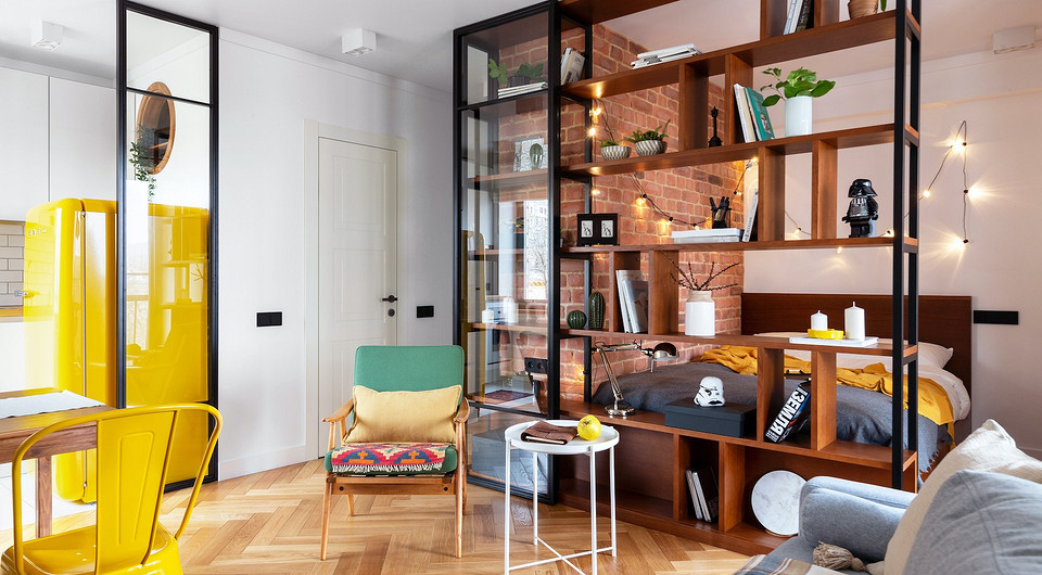 Большой стеллаж отделяет кухню-гостиную от спальни, чтобы создать в последней ощущение приватности. Возле стеллажа — небольшое винтажное кресло, в котором можно удобно устроиться и п...