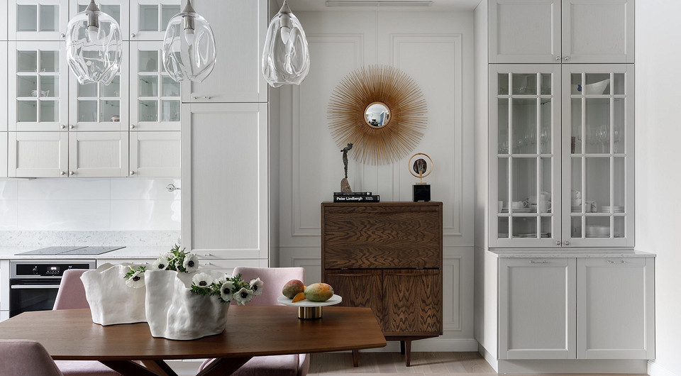 Кухонный гарнитур выполнен по индивидуальному заказу. Он вместительный, но выглядит в интерьере легко благодаря светлому оттенку. Отдельно от гарнитура стоит буфет, а между ними — деревян...