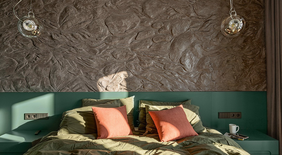 Несмотря на имитацию скальной породы — дань мужскому интерьеру — спальня смотрится уютно благодаря тёплым цветовым акцентам текстиля.