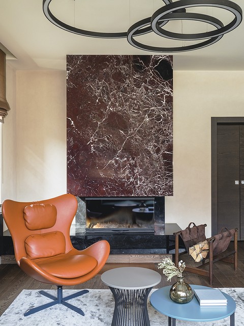 На светлом фоне стен в гостиной выделяется кресло в яркой обивке и камин, оформленный натуральным камнем. 
