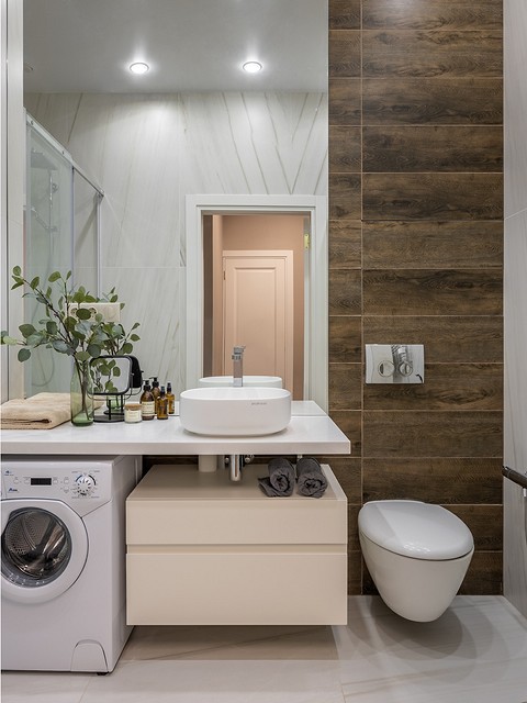 Часть стены в ванной комнате оформлена крупным зеркалом, которое визуально расширяет пространство. Этому же способствуют светлые стены с рисунком мрамора.