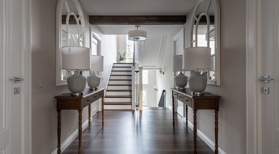 Холл второго этажа украшают симметричные консоли с настольными лампами и причудливыми зеркалами, напоминающими старинные окна с фигурным переплетом.
